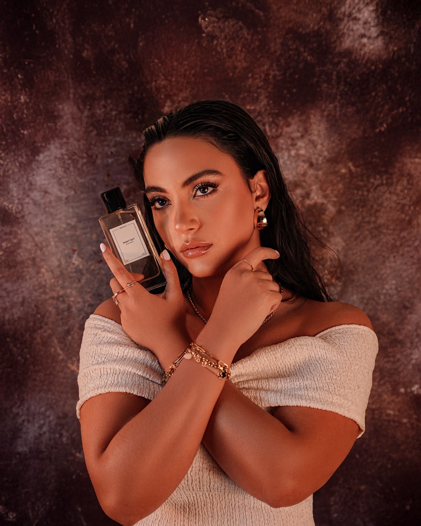Woman posing with a perfume bottle against a dramatic textured backdrop for fragrance beauty campaign photography.