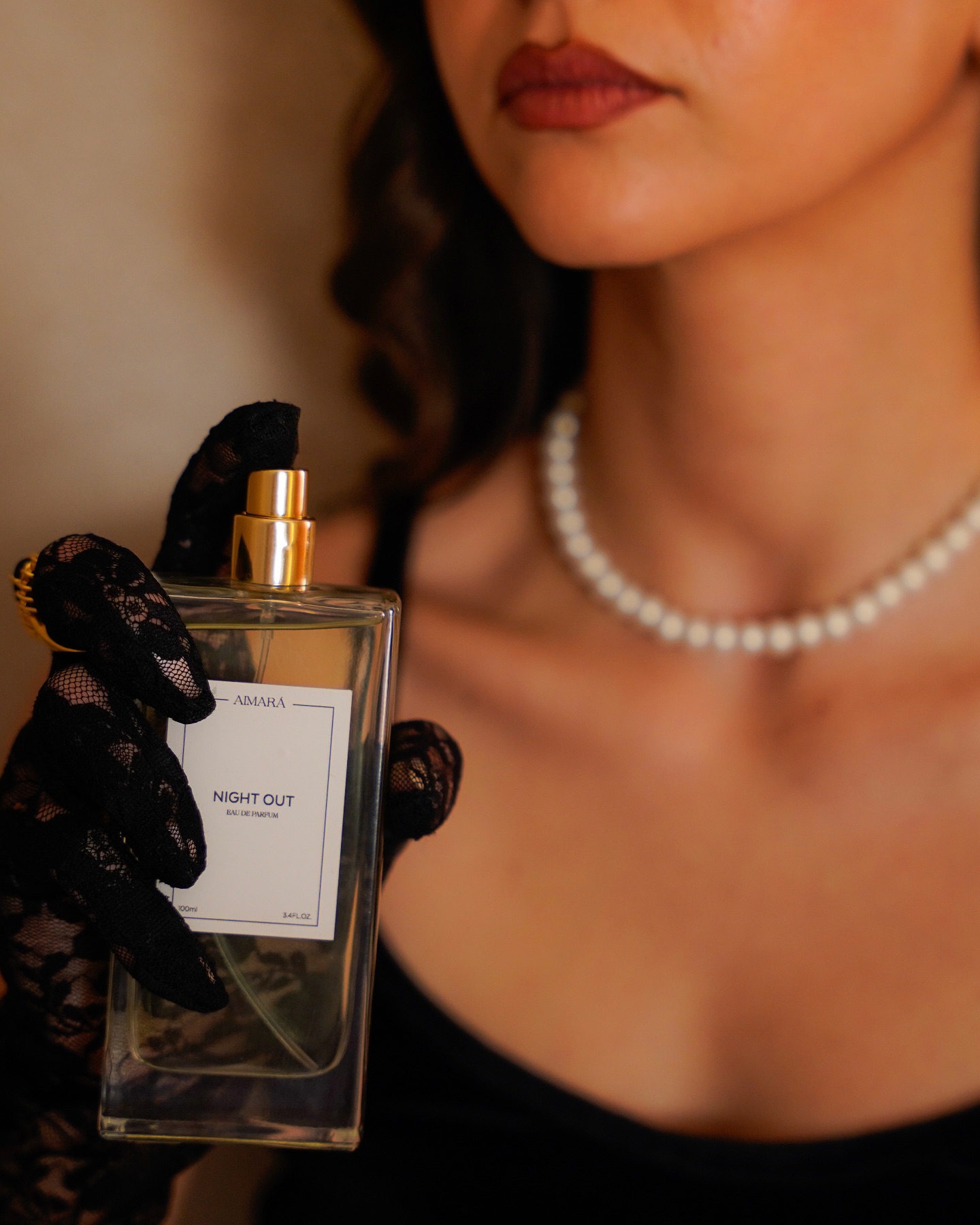 Woman in black gloves and pearl jewelry holding a perfume bottle in an elegant fragrance beauty photography scene.